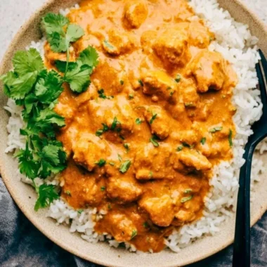 Delicious crockpot butter chicken served with rice and herbs.