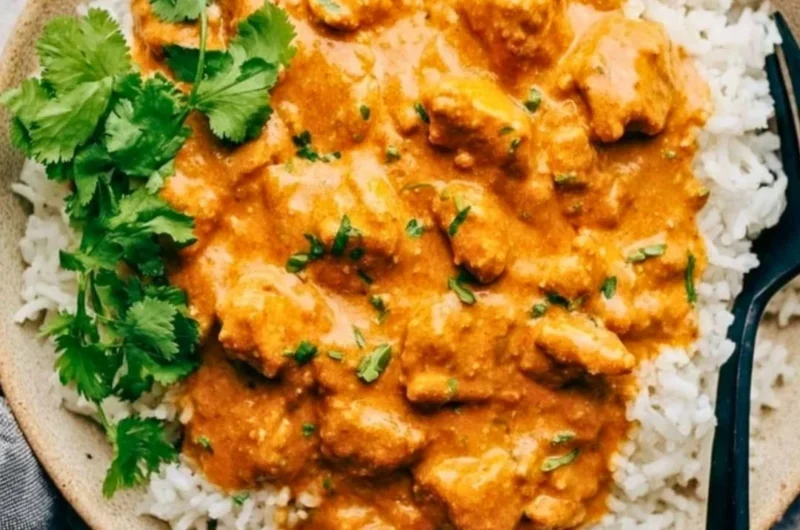 Delicious crockpot butter chicken served with rice and herbs.