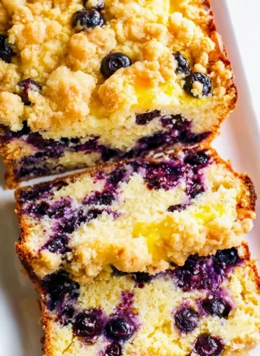 Delicious blueberry lemon loaf on a wooden table with fresh blueberries and lemons.