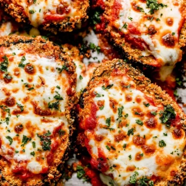 Crispy baked eggplant Parmesan served with fresh basil on a white plate.