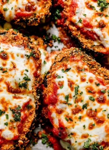 Crispy baked eggplant Parmesan served with fresh basil on a white plate.