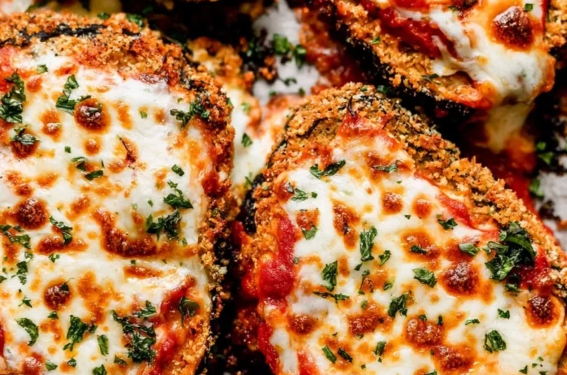 Crispy baked eggplant Parmesan served with fresh basil on a white plate.