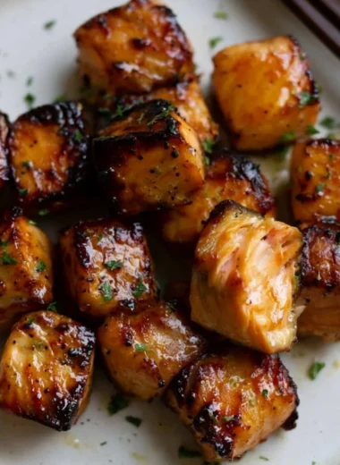 Air Fryer Honey Garlic Salmon Bites served on a plate garnished with herbs.